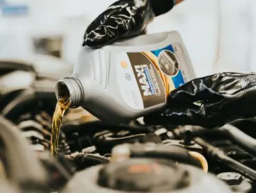 Close-up of a mechanic pouring engine oil into a car engine, highlighting maintenance work.